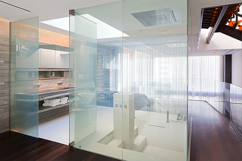 Smart glass panels enclose the master bathroom with its white Corian floor and sunken tub. Nothing interrupts the visual flow unless you touch the button that turns the clear panels opaque. 