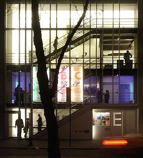 The wire-glass facade which shimmers as it reflects the sun becomes transparent at night. The people inside the theaterâ€™s foyer are perceived as â€œperformersâ€ when viewed from outside by passersby. This effect is created by four-story high linear lights hidden in the vertical â€œfoldsâ€ constructed between the walls of the foyers. The concealed lights illuminate the background, allowing the figures on the stairway to be seen in silhouette.